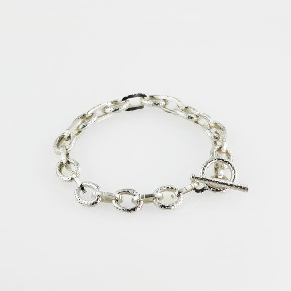 Textured round and flat oval sterling silver charm bracelet with a toggle clasp.