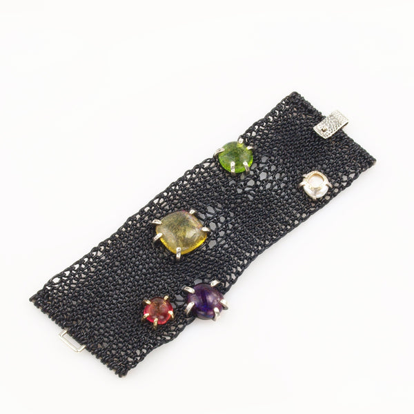 Knitted supple black leather bracelet with art glass cabochons set in Sterling silver and 14K yellow gold pong mountings with the strap lock partially visible.