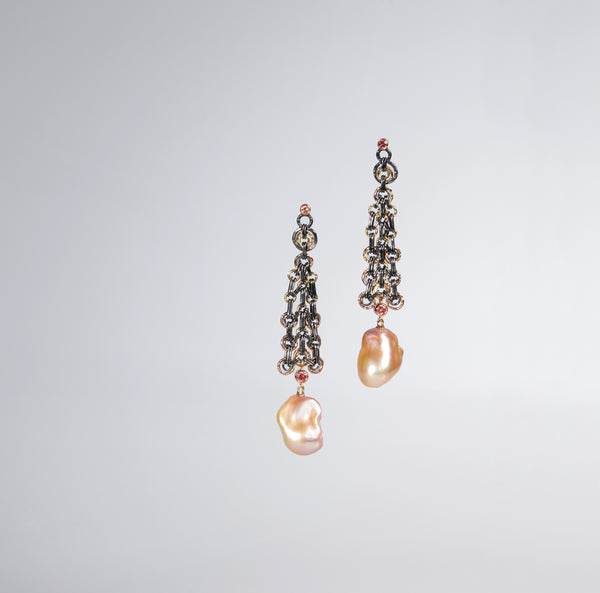 Long earrings in oxidized (black) silver with a giant peach colored oblong pearl at the bottom. colored gold accents and colored diamonds are also included.