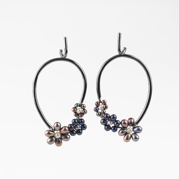 Three dark freshwater pearl flowers adorn the bottom of oxidized sterling silver pierced oval hoop earrings